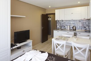 A compact kitchen with white cabinets, a tiled backsplash, a coffee maker, and a dining area with white chairs. - Paradiso Apartcomplex (Nessebar)