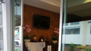 A seating area with wooden chairs and tables, a brick wall, a mounted television, and potted plants. - Chinotel (Phuket)