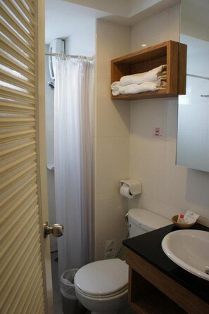 Un baño con inodoro, lavamanos, cortina de ducha y estante para toallas.