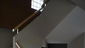 A staircase with white steps and a wooden handrail, leading to a landing with a dark wall and two framed pictures. - Chinotel (Phuket)