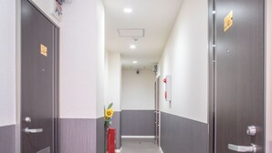 Un couloir avec deux portes de chaque côté, un extincteur rouge et une plante au centre.
