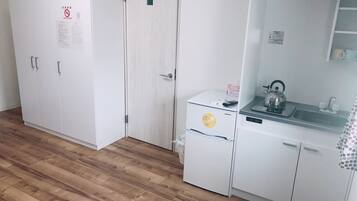 A compact room with a wardrobe, a small kitchenette, and a door with a 'No Smoking' sign.