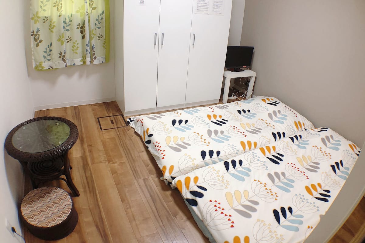 Una habitación pequeña con cama, armario, una mesita y un taburete.
