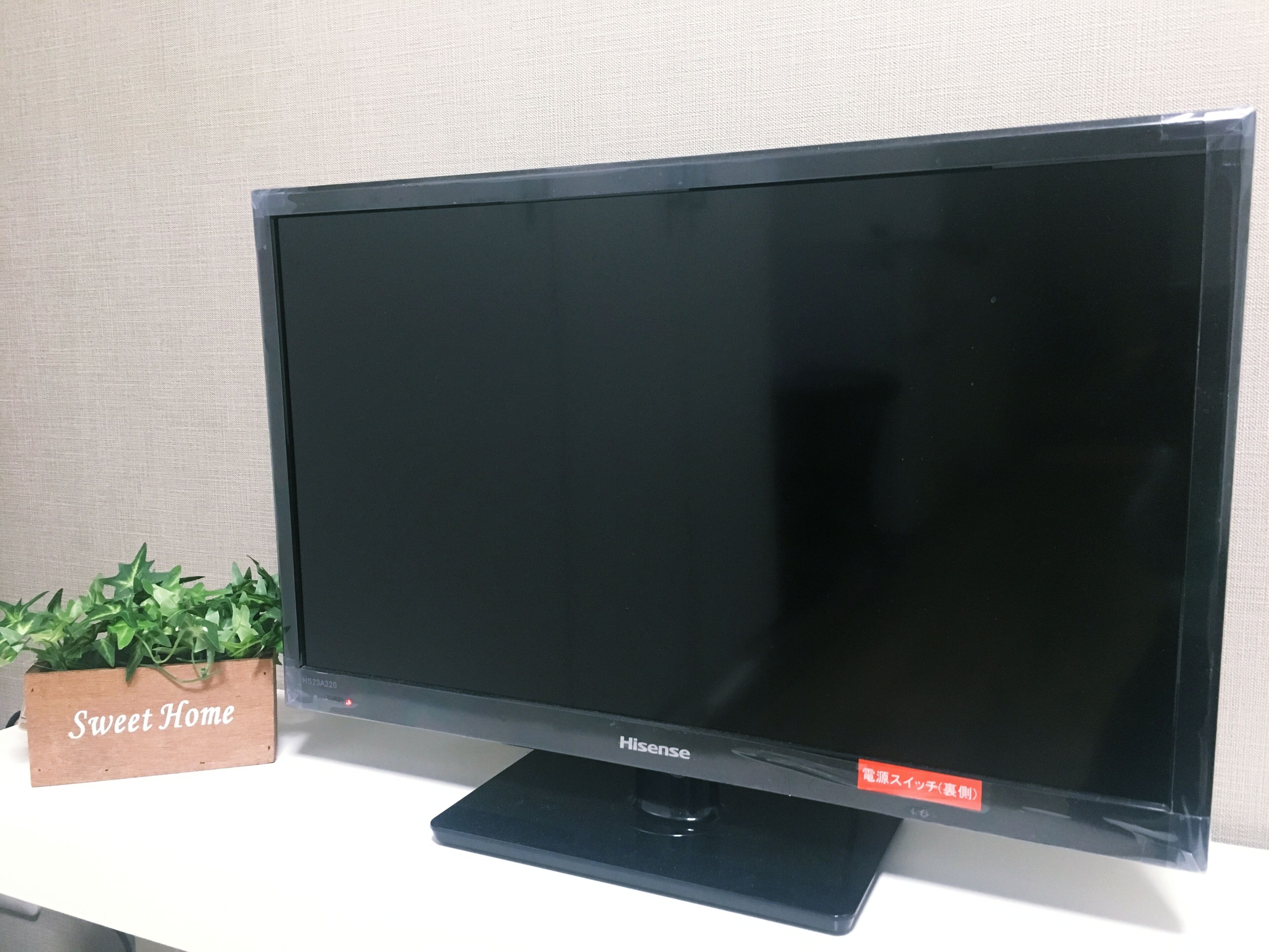 A flat-screen TV on a stand with a wooden sign labeled 'Sweet Home' beside it.