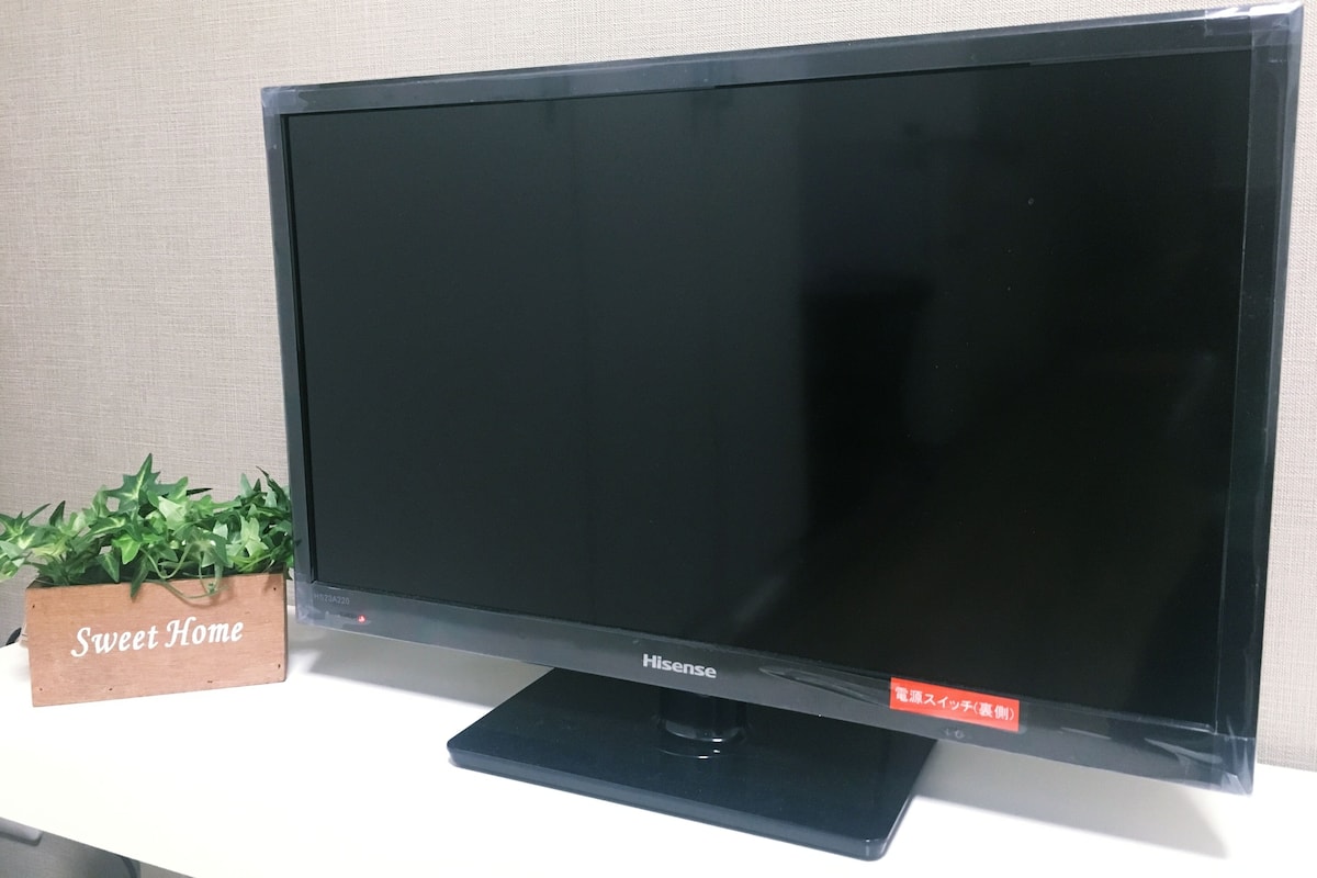 Un televisor de pantalla plana sobre un soporte, con un letrero de madera que dice 'Sweet Home' a su lado.