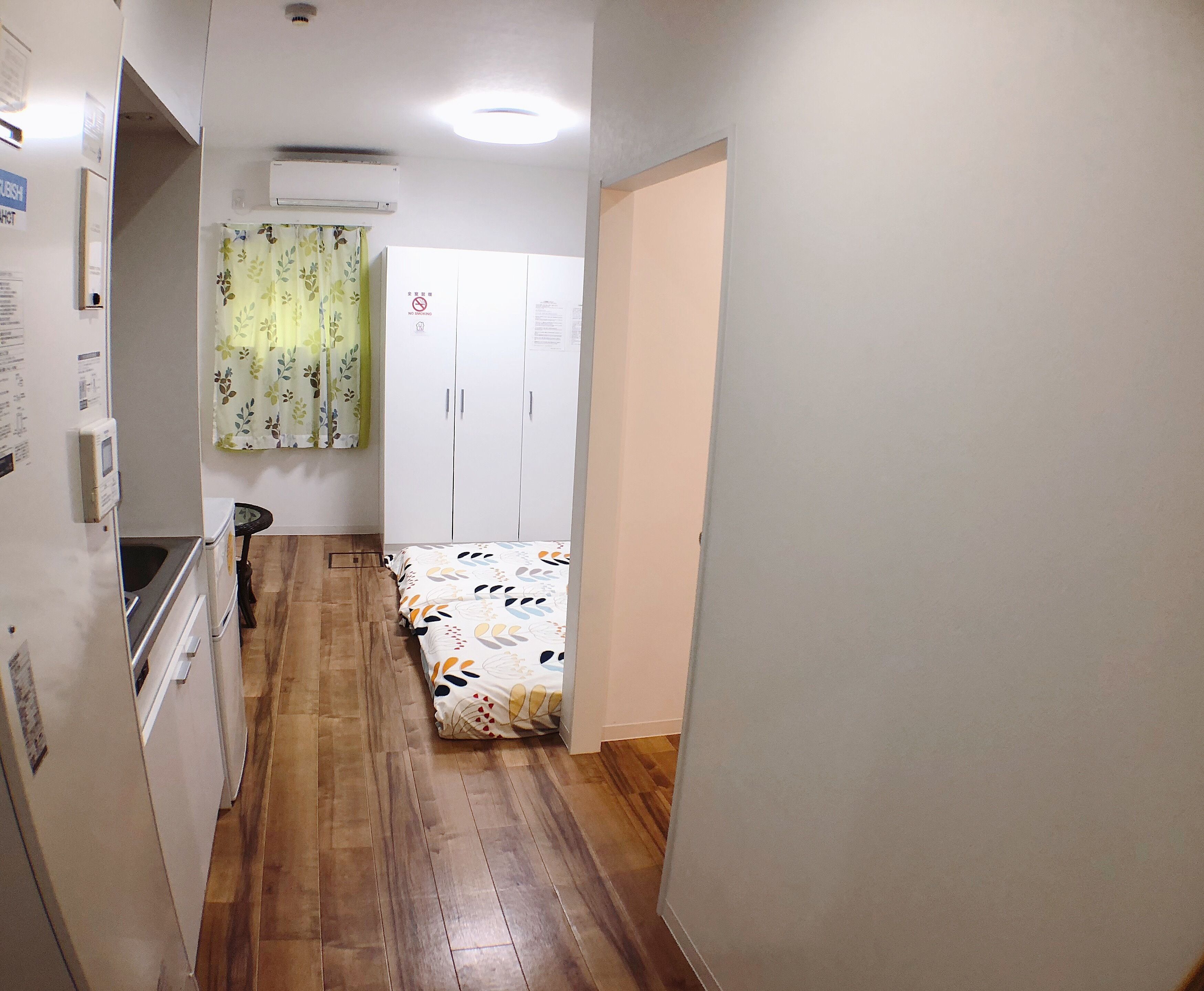 A narrow hallway with wooden flooring leading to a bedroom with a bed and a wardrobe.