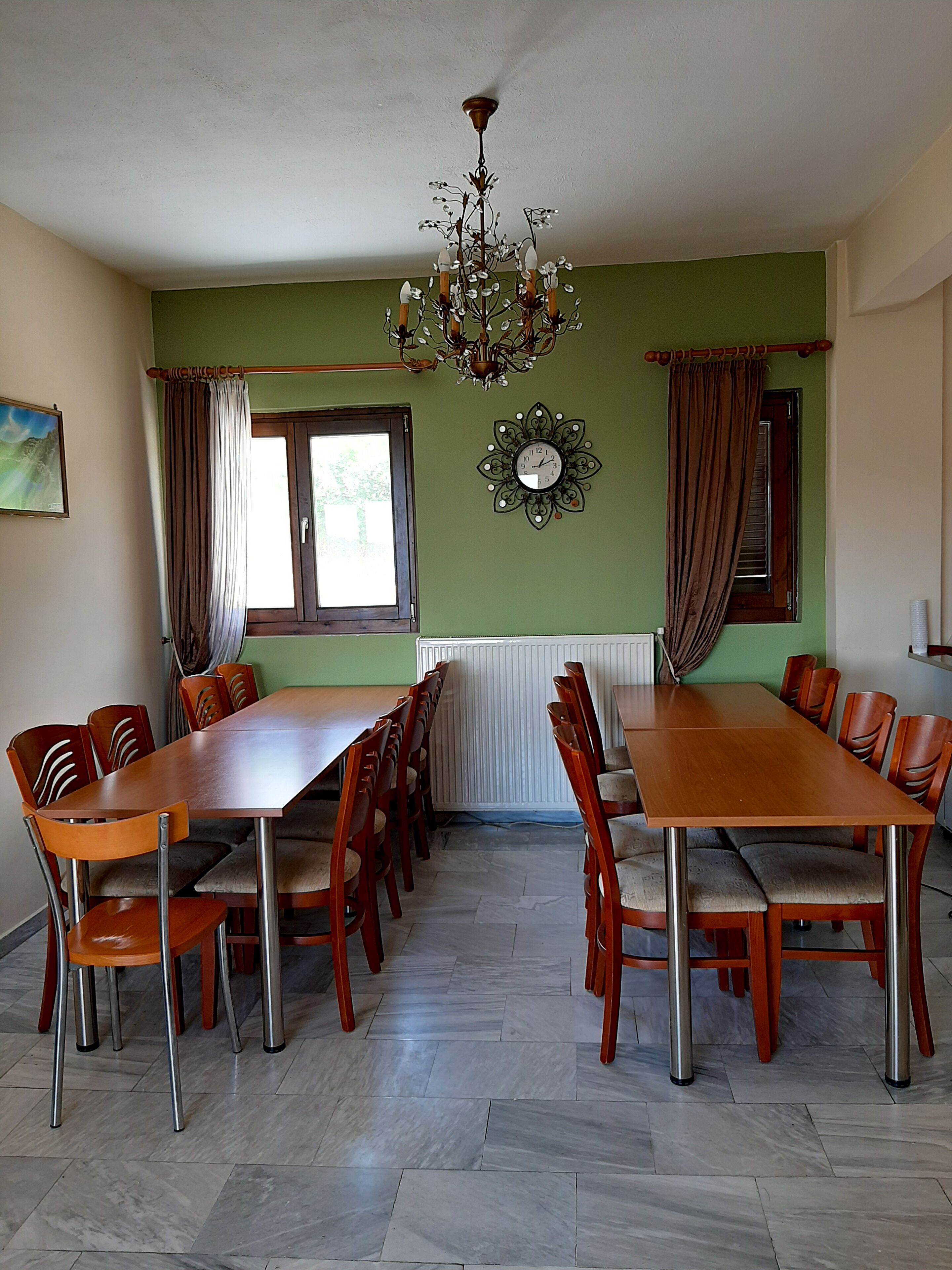 Comedor con una larga mesa de madera y sillas, un candelabro, un reloj y un ventanal con cortinas.