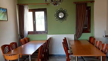 Comedor con una larga mesa de madera y sillas, un candelabro, un reloj y un ventanal con cortinas.