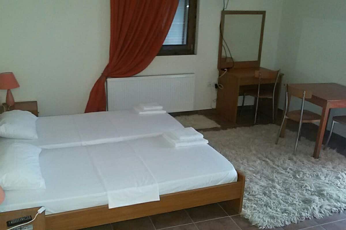 Ein Schlafzimmer mit Bett, Schreibtisch, Stuhl, Lampe und einem Fenster mit Vorhängen.