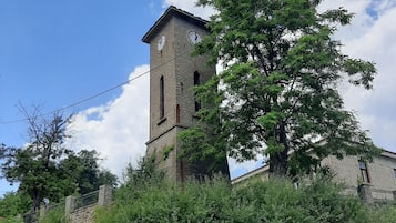 Une tour de pierre historique, surmontée d’une horloge, entourée d’une végétation luxuriante et s’élevant vers un ciel dégagé.