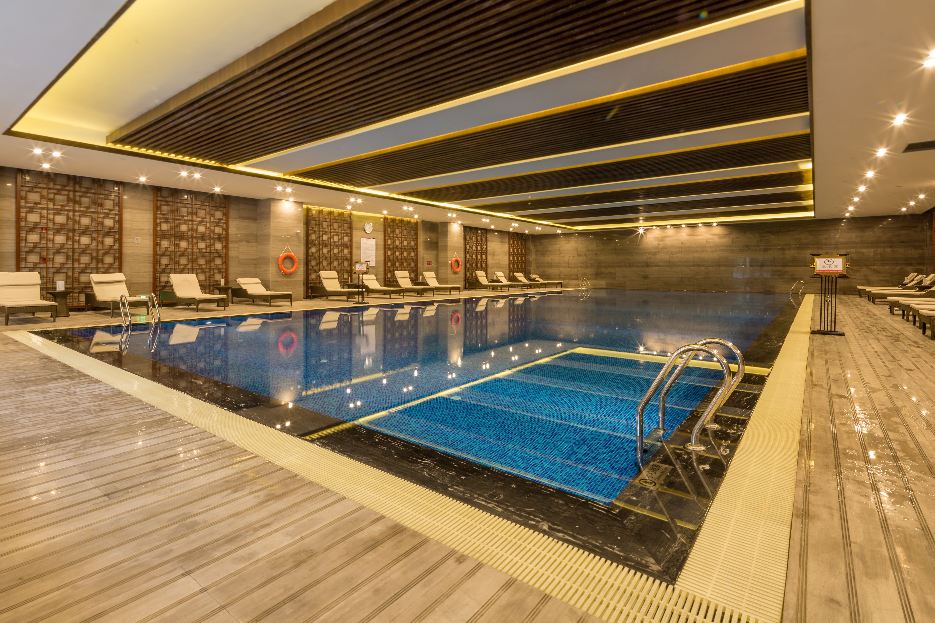 A modern indoor swimming pool with lounge chairs and a lifeguard stand.