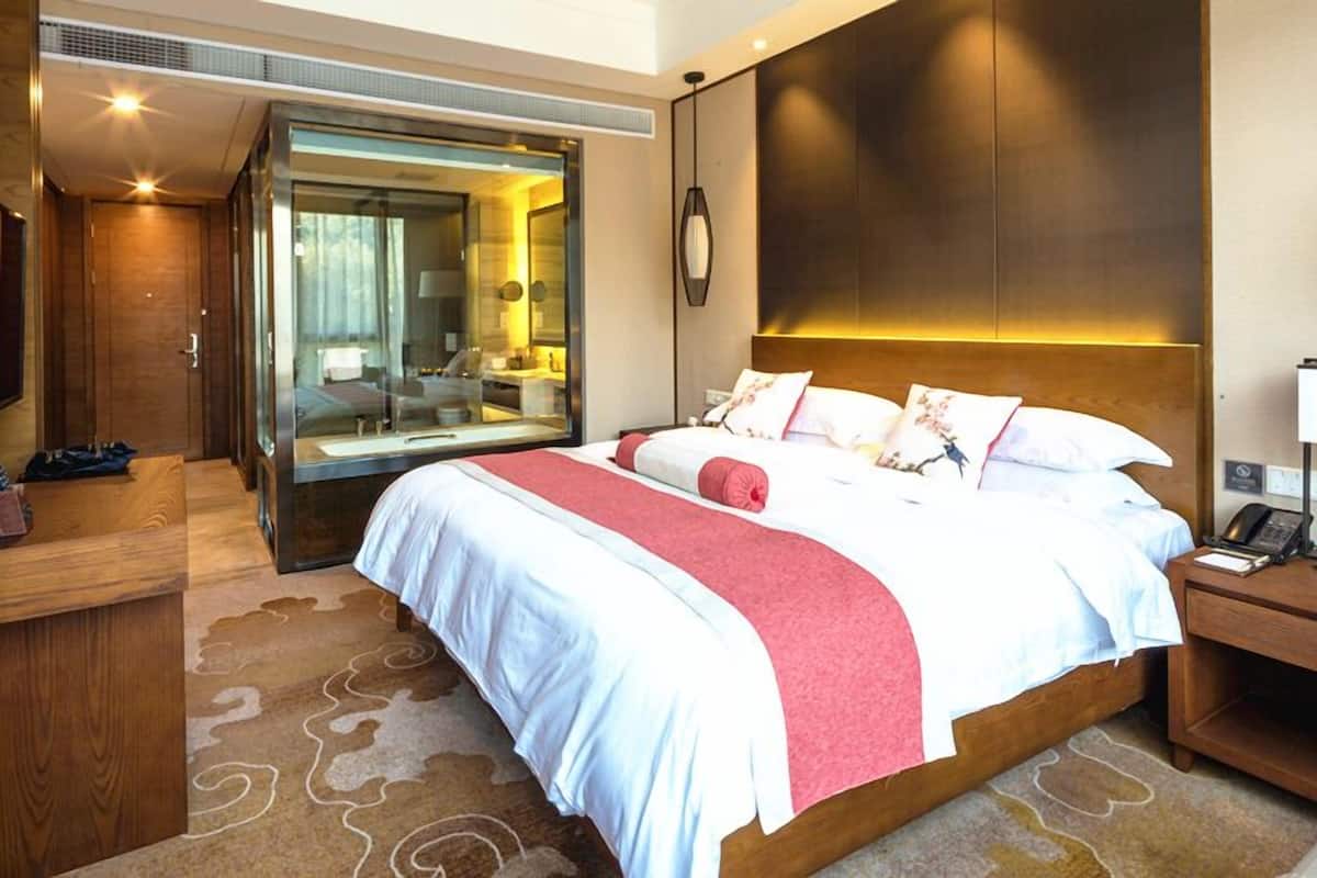 Ein modernes Hotelzimmer mit einem großen Bett, einem in Glas eingefassten Badezimmer und einem Holzkopfende.