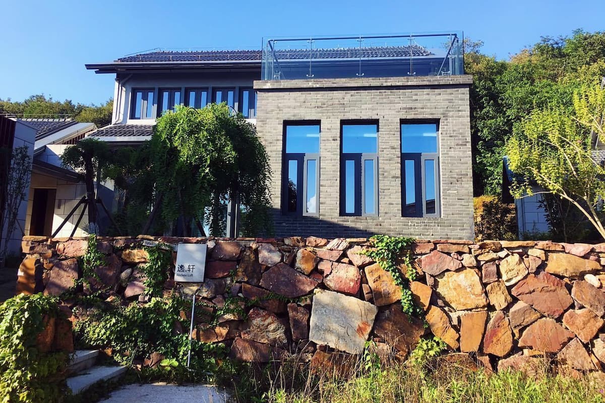 Ein modernes, zweistöckiges Haus mit einer Steinwand und blauem Himmel. Ein Schild trägt die Aufschrift 'Richer Life'.