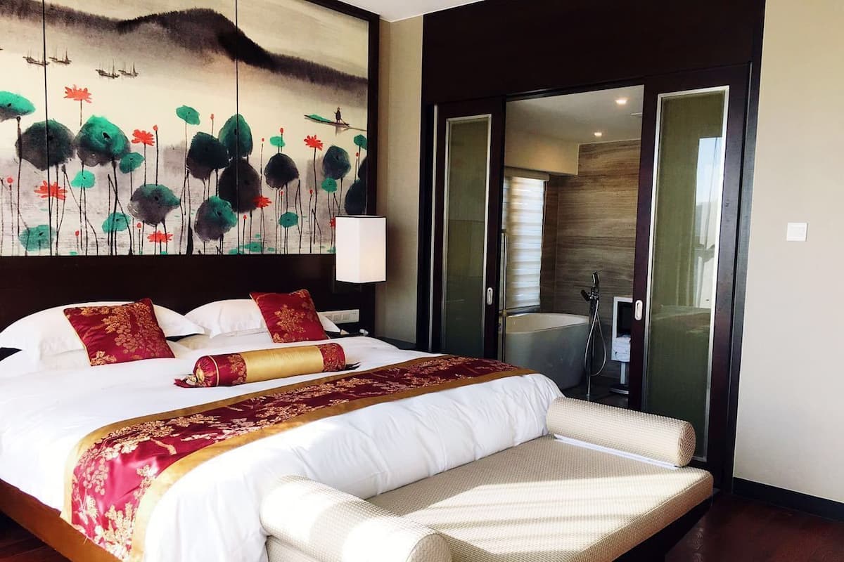 Ein Hotelzimmer mit einem großen Bett, einem Bild an der Wand und einer Schiebetür zum Badezimmer.