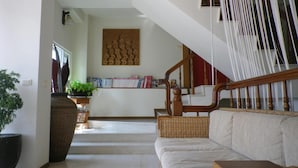 A spacious living area with a staircase, a sofa, a large plant, and a bookshelf. - MaMaLuLu Hostel (Hengchun)