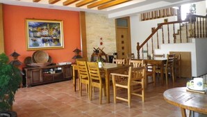 A dining area with a wooden table and chairs, a painting on the wall, and a staircase leading to an upper level. - MaMaLuLu Hostel (Hengchun)