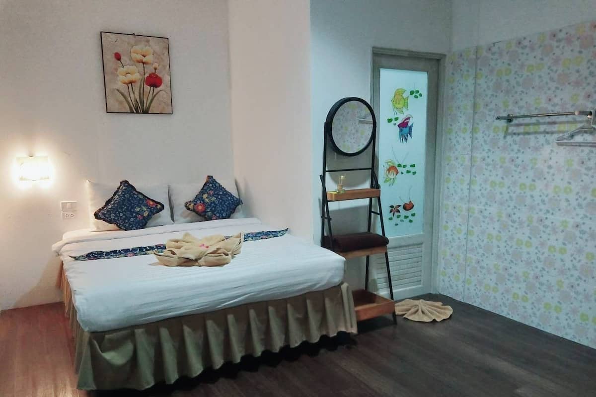 Un dormitorio con una cama, almohadas, una mesita de noche, un espejo y una pared con estampado floral.