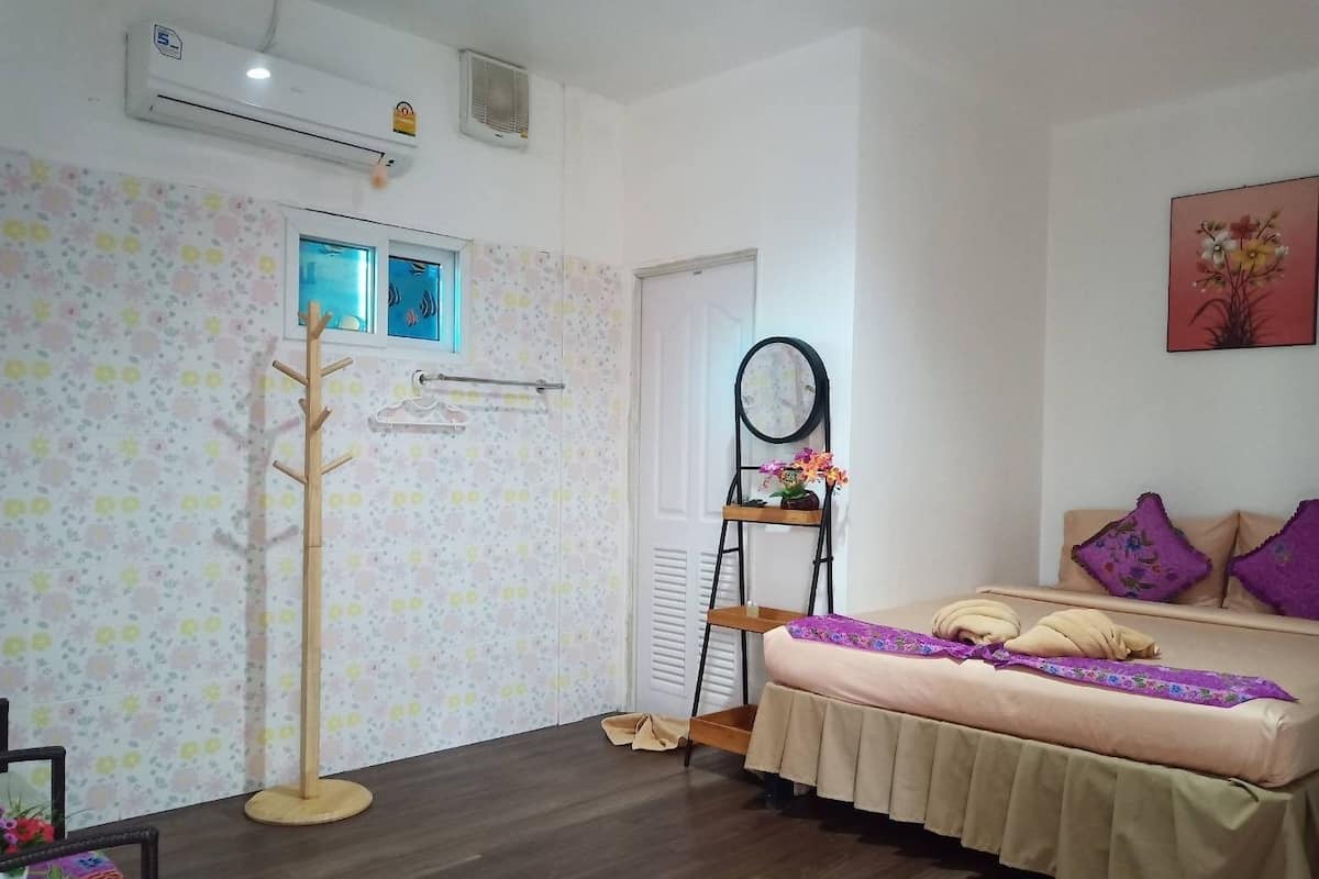 Un dormitorio con cama, perchero de madera, espejo y ventana.