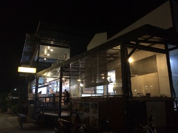 A restaurant with a glass enclosure, outdoor seating, and a visible kitchen area. - Decho Hostel (Koh Lipe)
