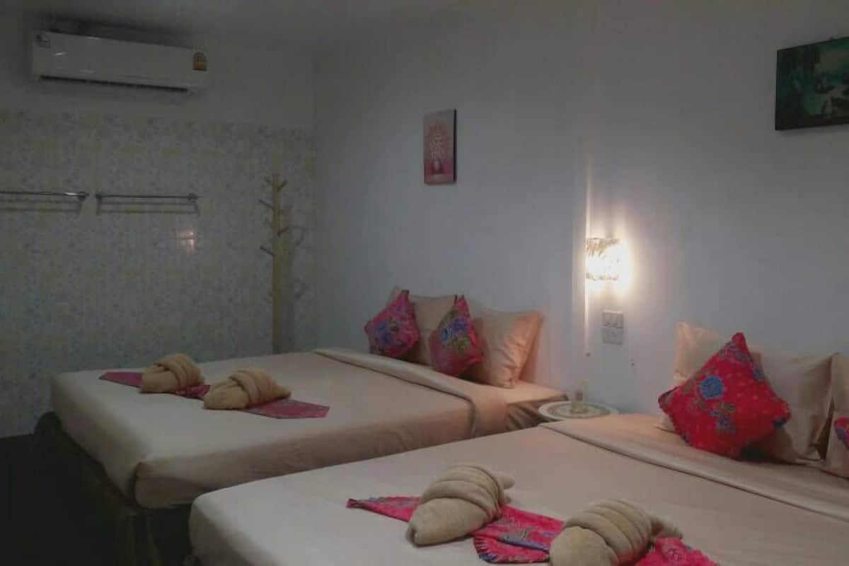 Habitación de hotel con dos camas, cada una con almohada y toalla. Hay un aire acondicionado instalado en la pared y una mesita con una lámpara.