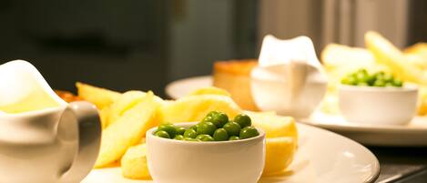 A plate of food with peas and potatoes, and a jug of sauce.