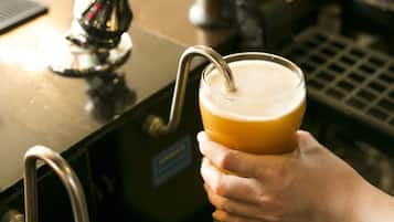 Una mano sosteniendo una jarra de cerveza con una pajita, cerca de una llave y un grifo.