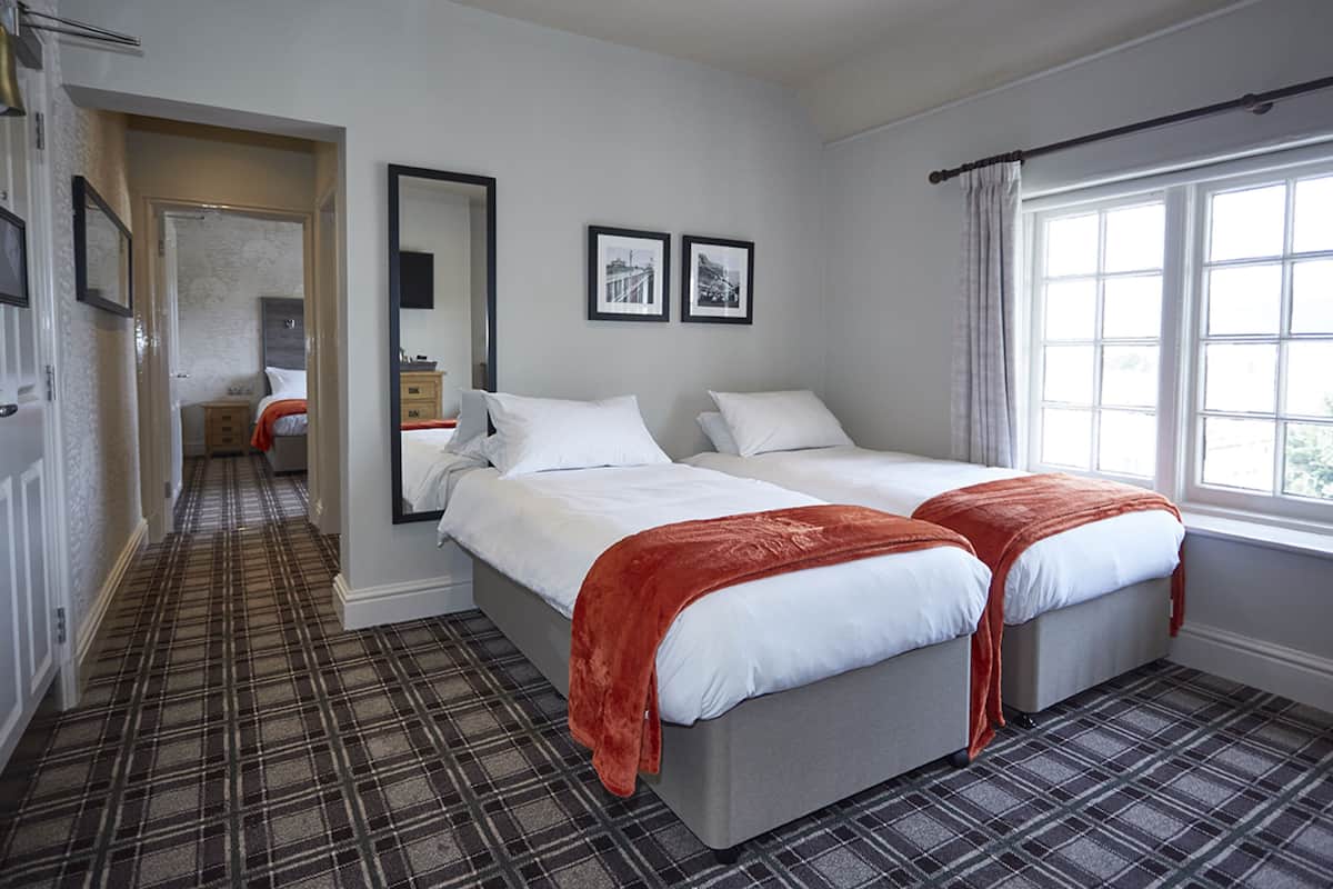 Een hotelkamer met twee bedden, een groot raam, een spiegel en een deur naar een andere kamer.