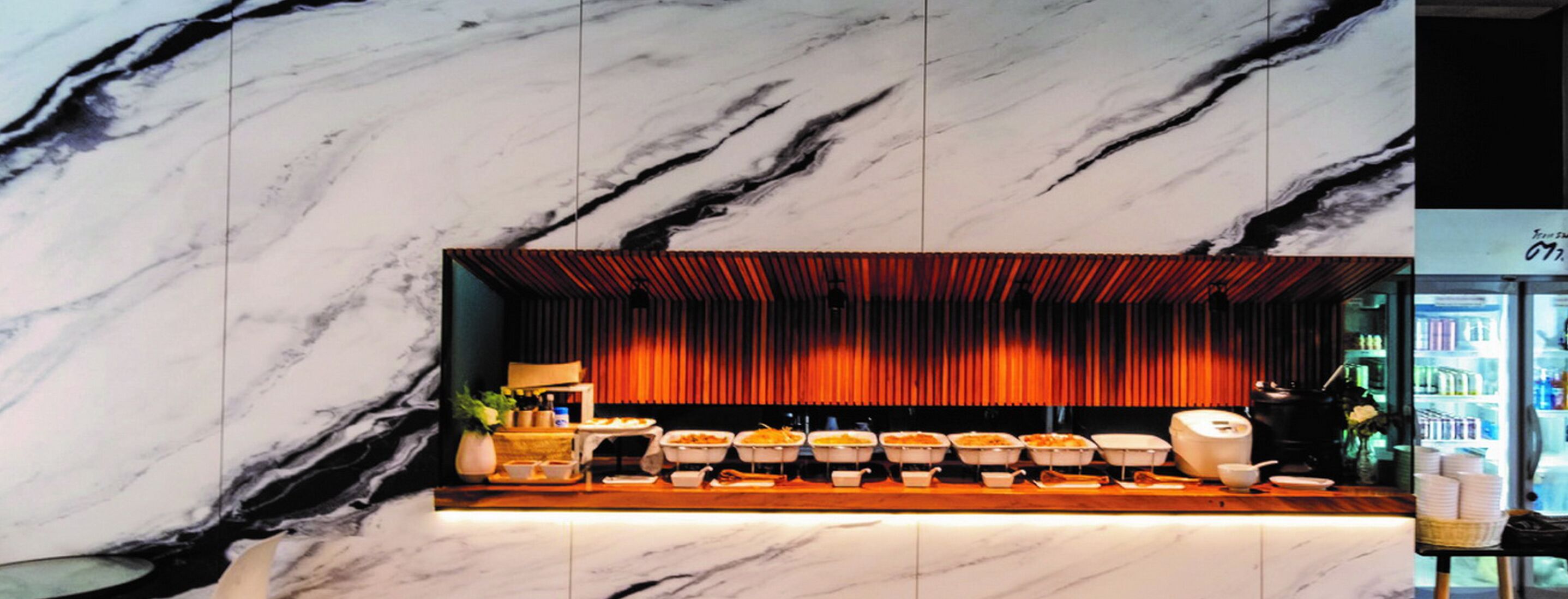 Pared de mármol con una barra de buffet que presenta diferentes platos y un telón rojo de fondo.