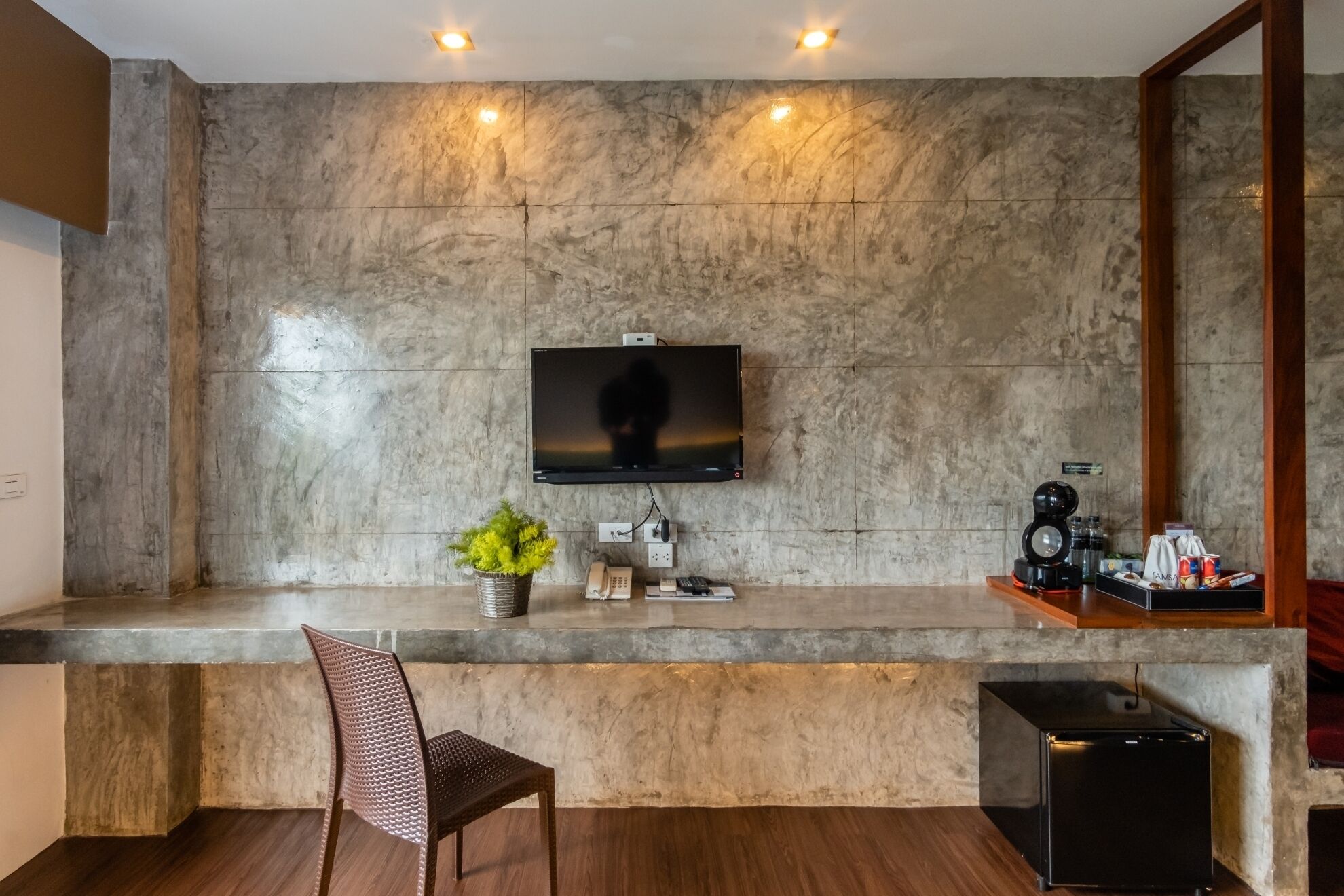 Una sala de estar moderna con un televisor de pantalla plana montado en una pared texturizada, una mesa de centro de madera, un sillón y un altavoz negro pequeño.