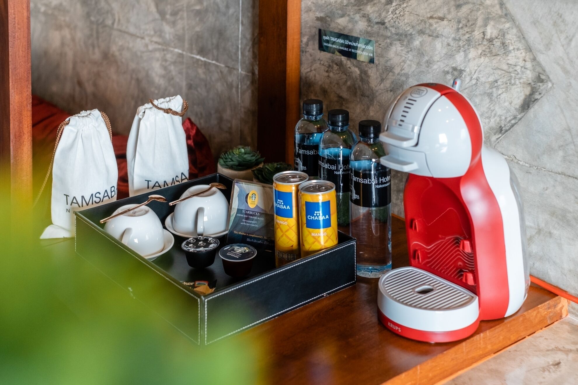 A tray with tea sets, cans of beverages, and a red and white coffee machine on a wooden surface.