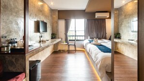 A modern hotel room with a large bed, a desk with a flat-screen TV, a chair, and a small table.