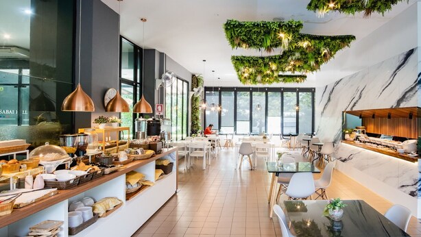 A modern dining area with a buffet setup, large windows, and a ceiling with hanging greenery.