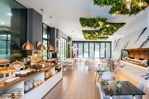 Un espace repas moderne, doté d’un buffet, de grandes fenêtres et d’un plafond orné de plantes suspendues.