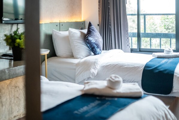 Habitación de hotel con dos camas, una mesita de noche, una planta en maceta y una ventana con cortinas.