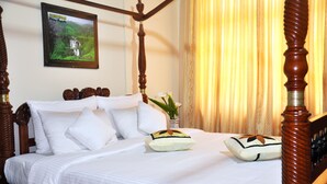 Una cama con dosel, ropa de cama blanca y almohadas decorativas, un cuadro en la pared y un florero con flores sobre la mesita de noche.