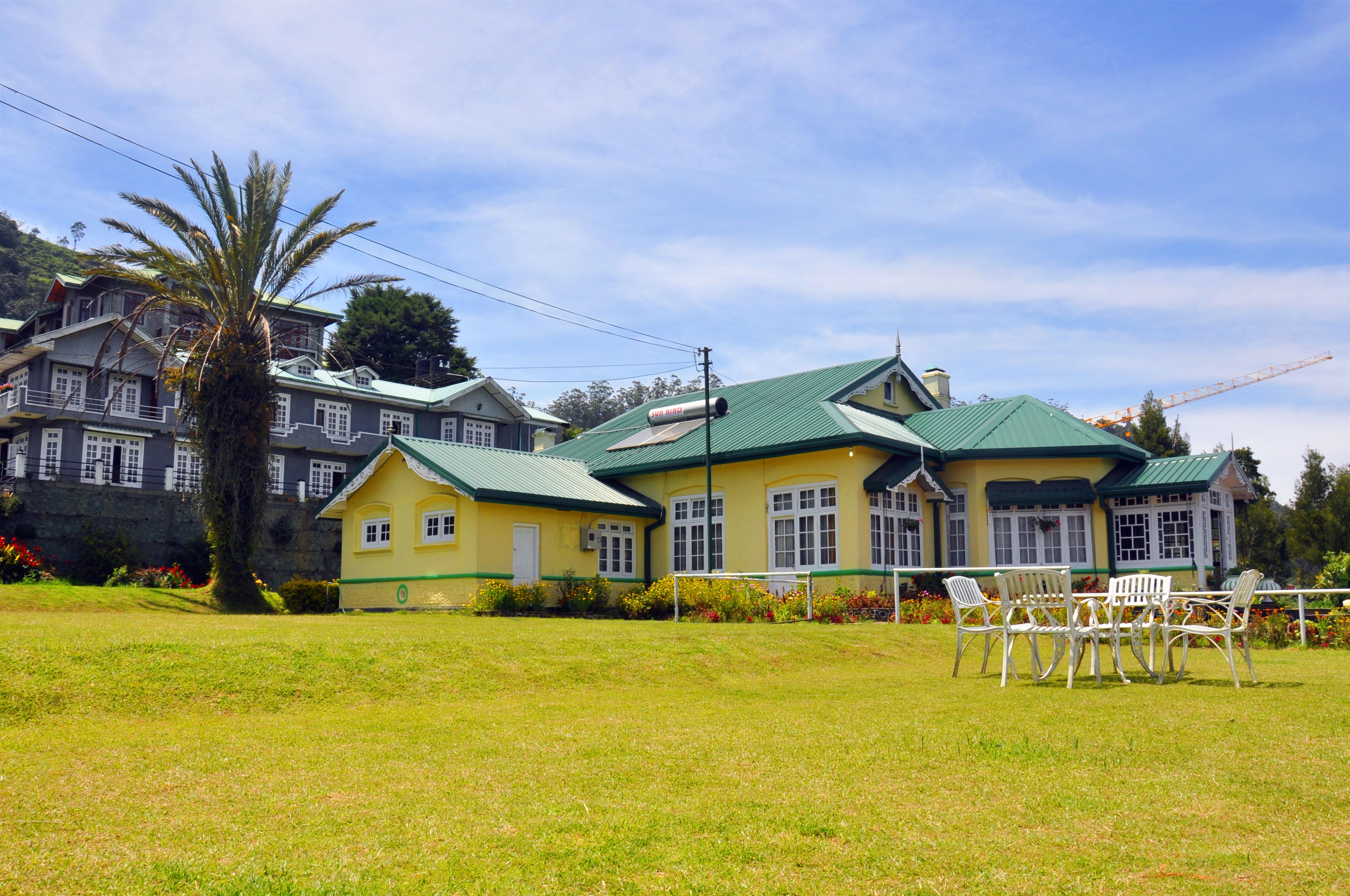 A two-story building with a green roof, a balcony, and a lawn with chairs.