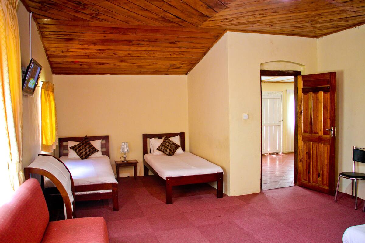 A room with two wooden beds, a red chair, a wooden door, and a wooden ceiling.