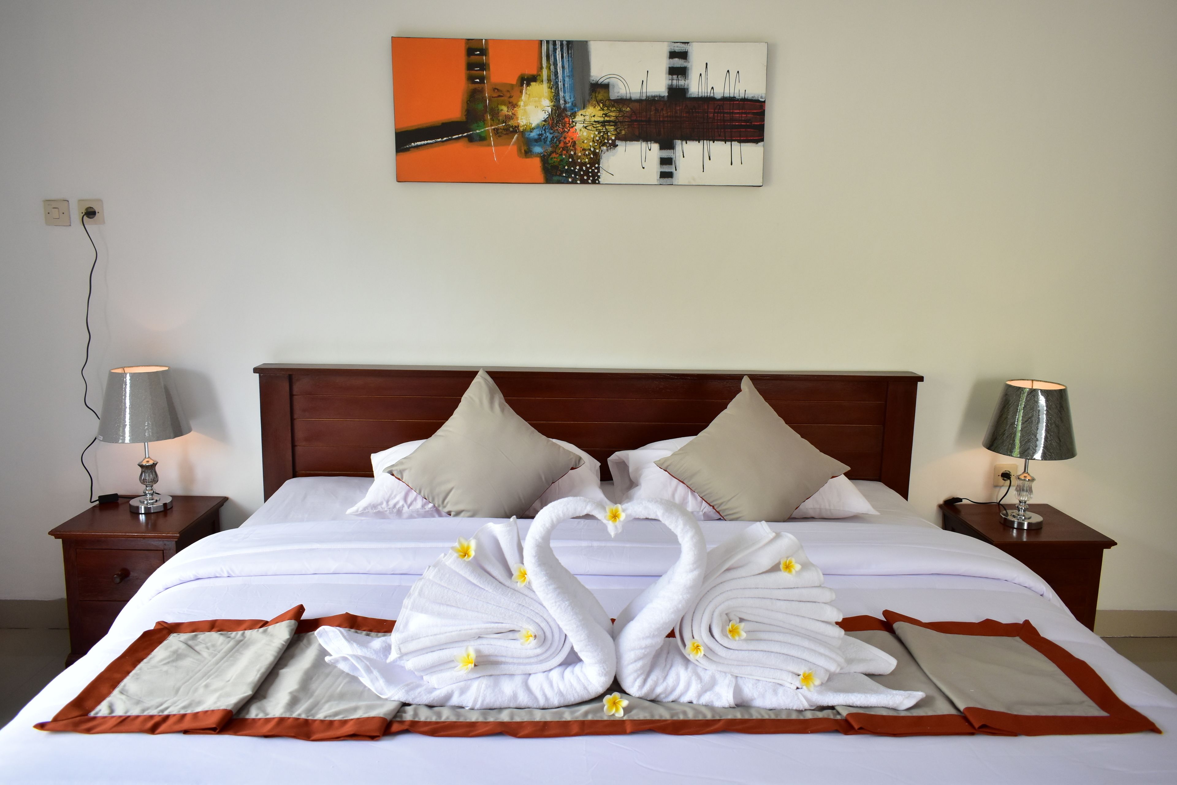 Cama arrumada com lençóis brancos, dois travesseiros e uma decoração de toalhas em formato de cisne. Há duas mesas de cabeceira com abajures.