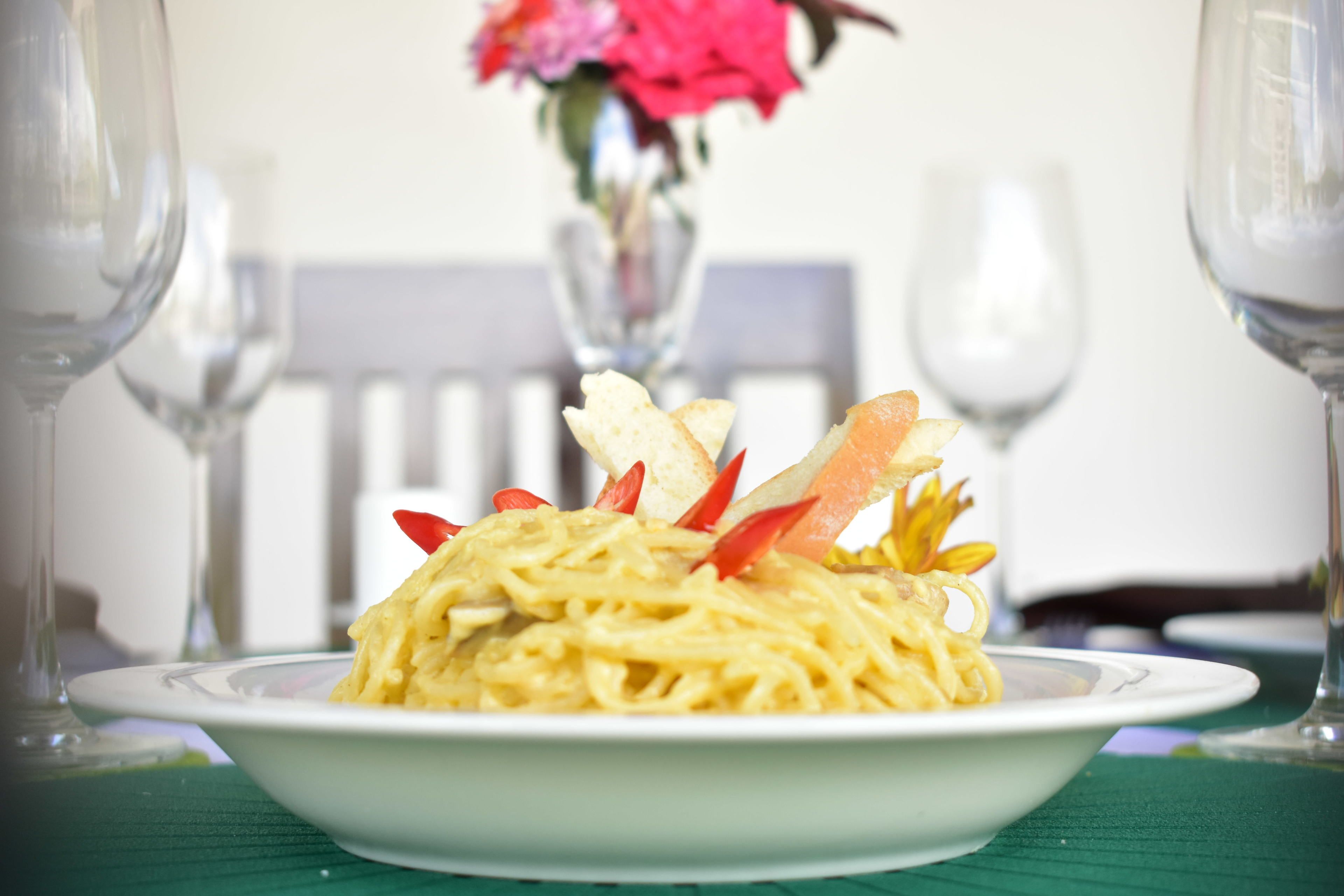 A plate of pasta garnished with vegetables and fruit, placed on a table with a green tablecloth.