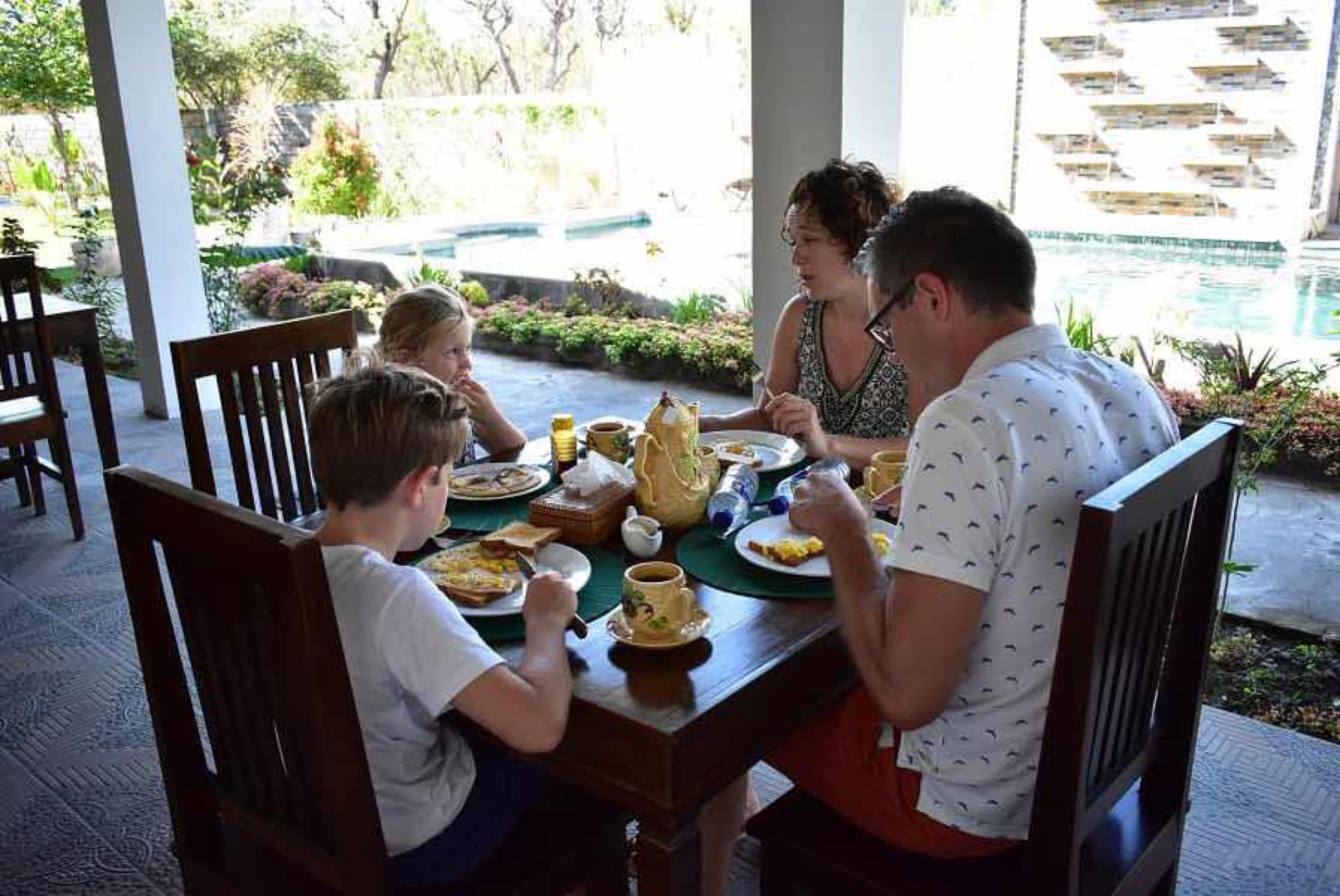 Una familia cenando en una mesa al aire libre con vista a la piscina.