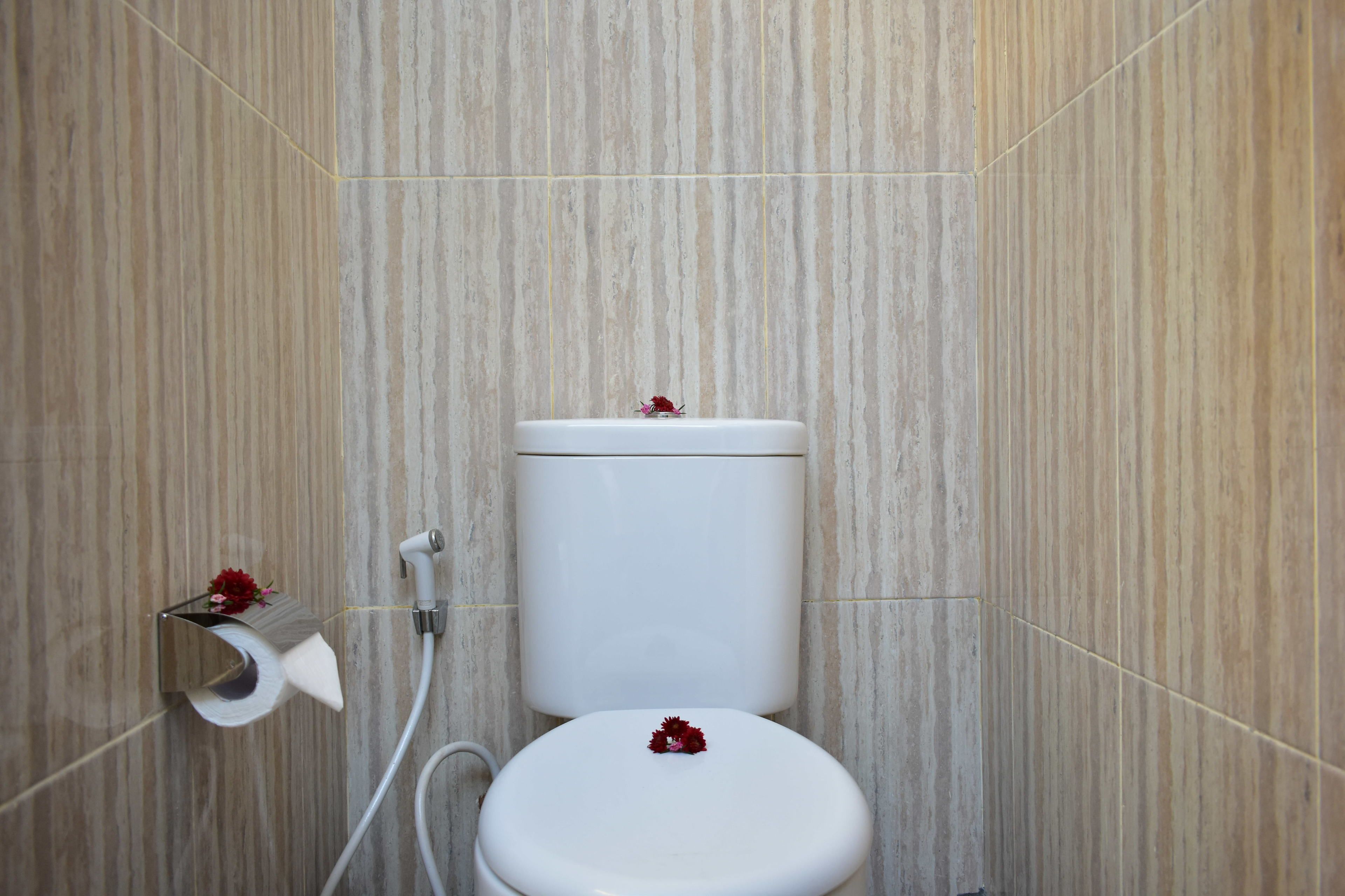 Un inodoro con tanque y asiento blancos, un porta papel higiénico con un rollo, y una flor sobre el asiento.