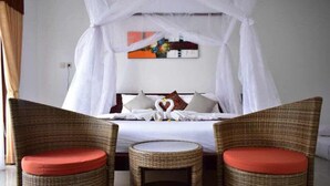 Ein Schlafzimmer mit einem Bett, zwei Korbstühlen mit roten Kissen und einem Baldachin.