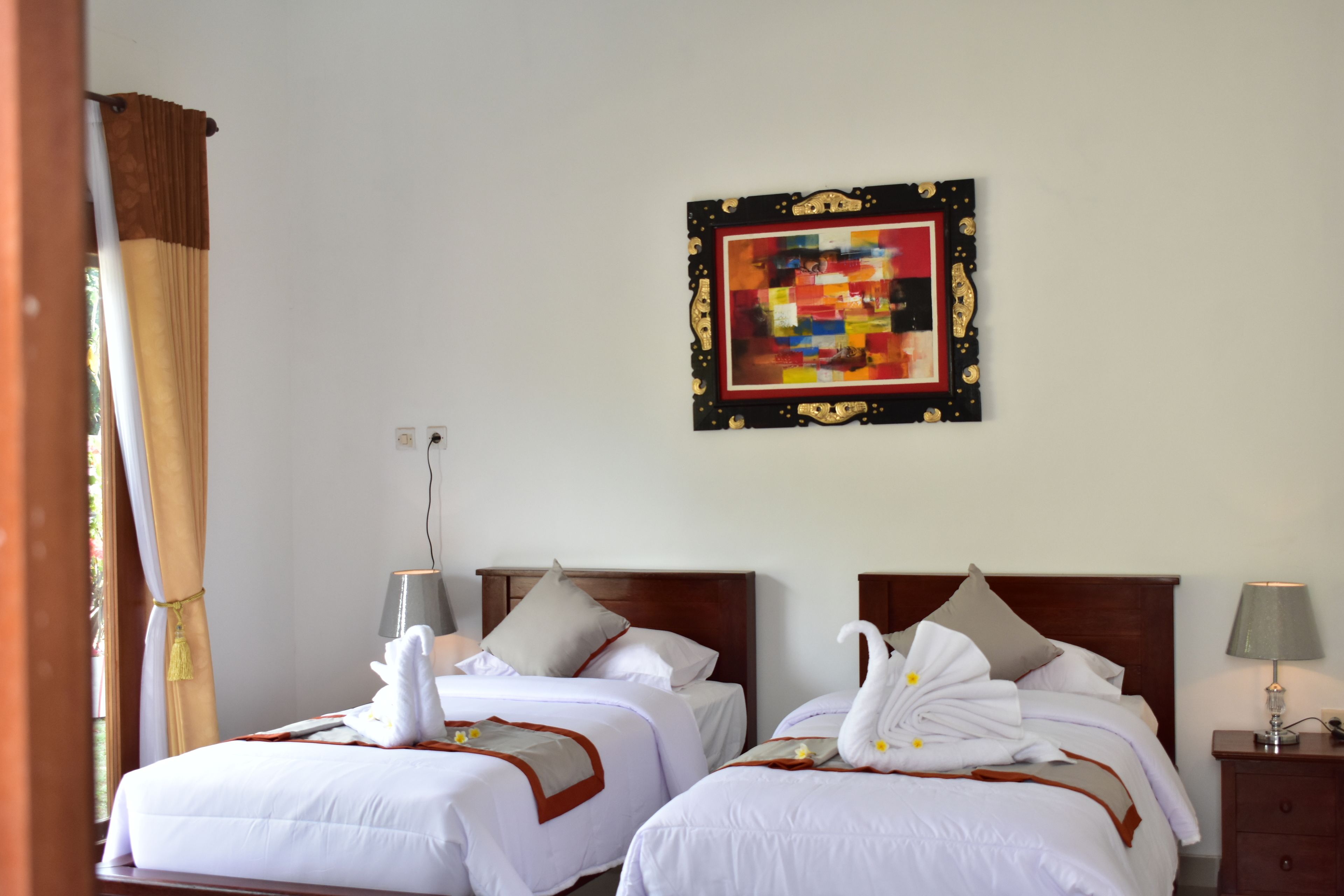 Habitación de hotel con dos camas, cada una con ropa de cama blanca y una decoración de toallas con forma de cisne. Hay una obra de arte colgada en la pared sobre las camas y una mesita de noche con una lámpara.