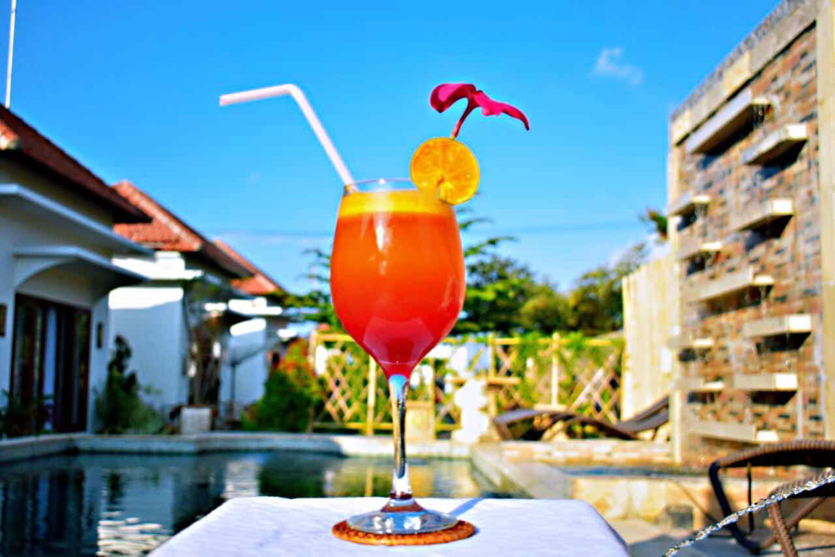 A cocktail with a straw and a garnish on a table by a poolside.