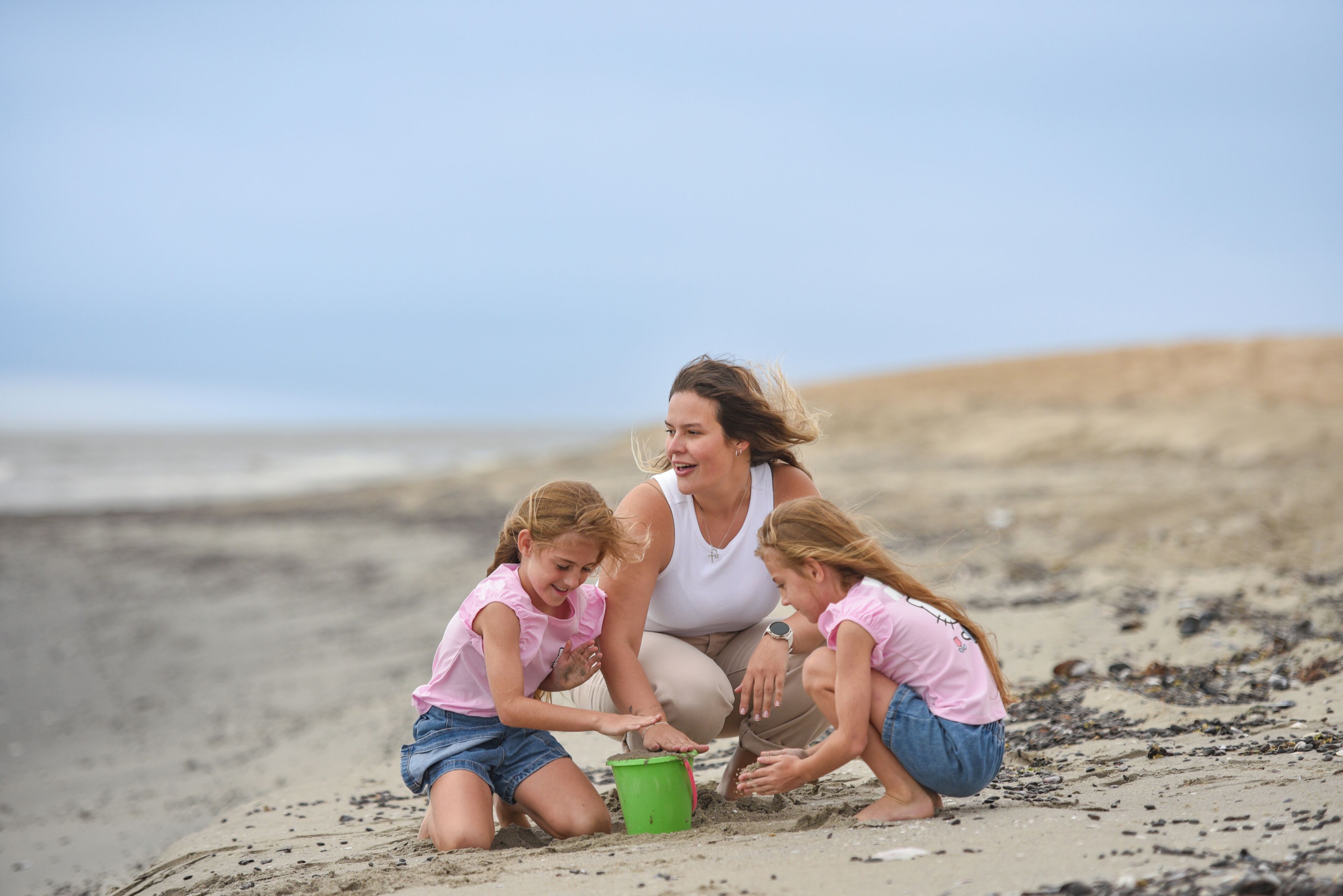 Une femme et deux enfants jouent dans le sable sur une plage.
