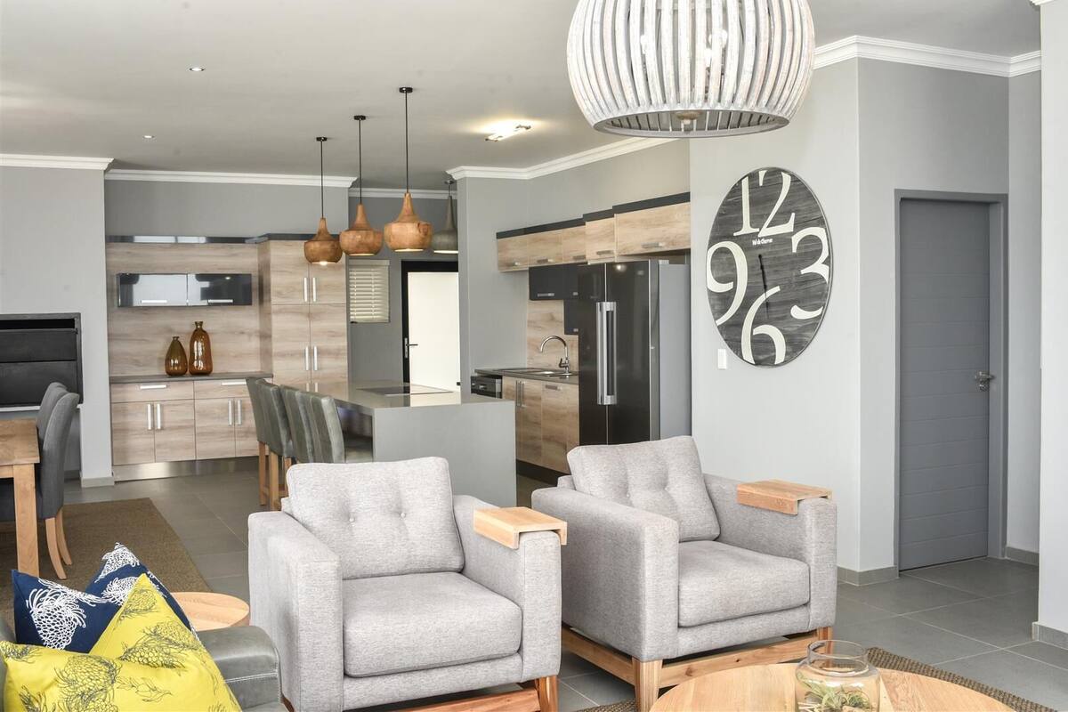 A modern living room with grey sofas, a wooden coffee table, and a large wall clock.