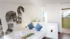 Ein modernes Hotelzimmer mit einem großen Bett, weißen Leintüchern, blauen Kissen, einem Nachttisch mit Tasse und einem Spiegel über dem Bett.