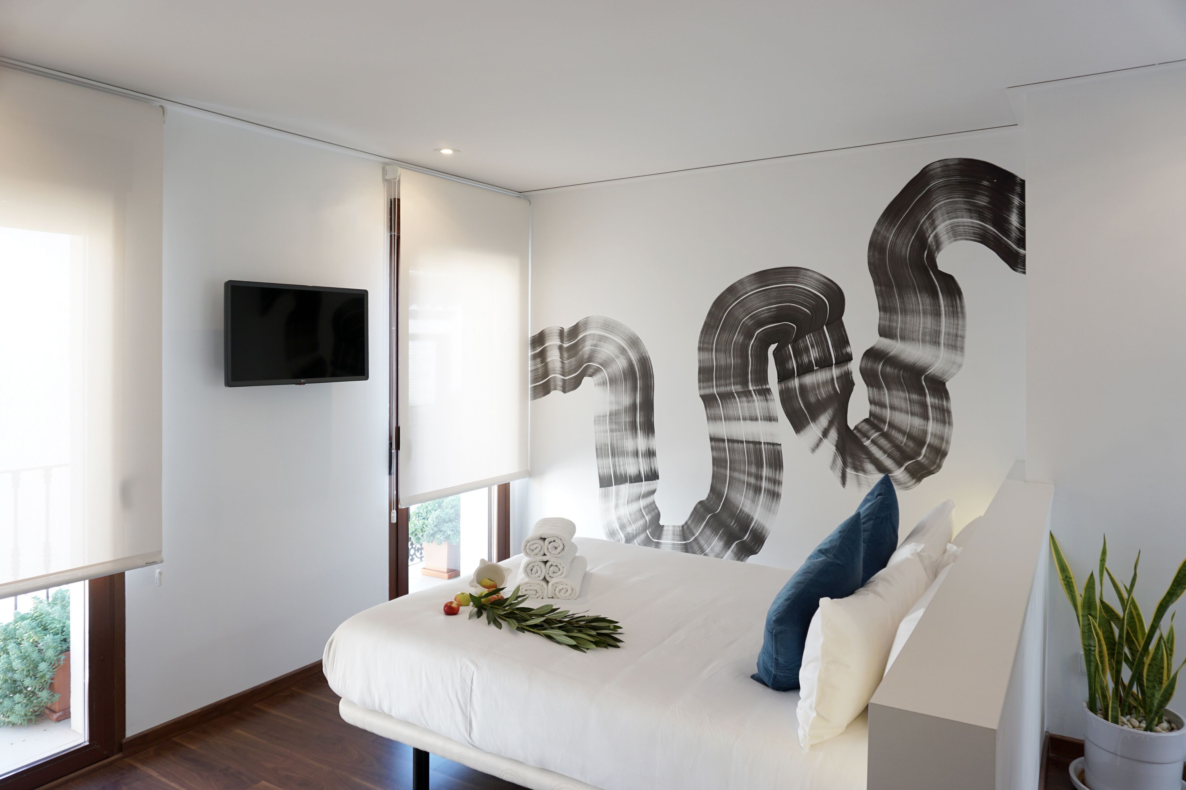 Un dormitorio moderno con una cama grande, un televisor de pantalla plana y una pieza de arte original en la pared.