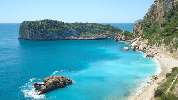 Eine Küstenlandschaft mit einer felsigen Insel, klarem türkisblauem Wasser und einem Sandstrand.