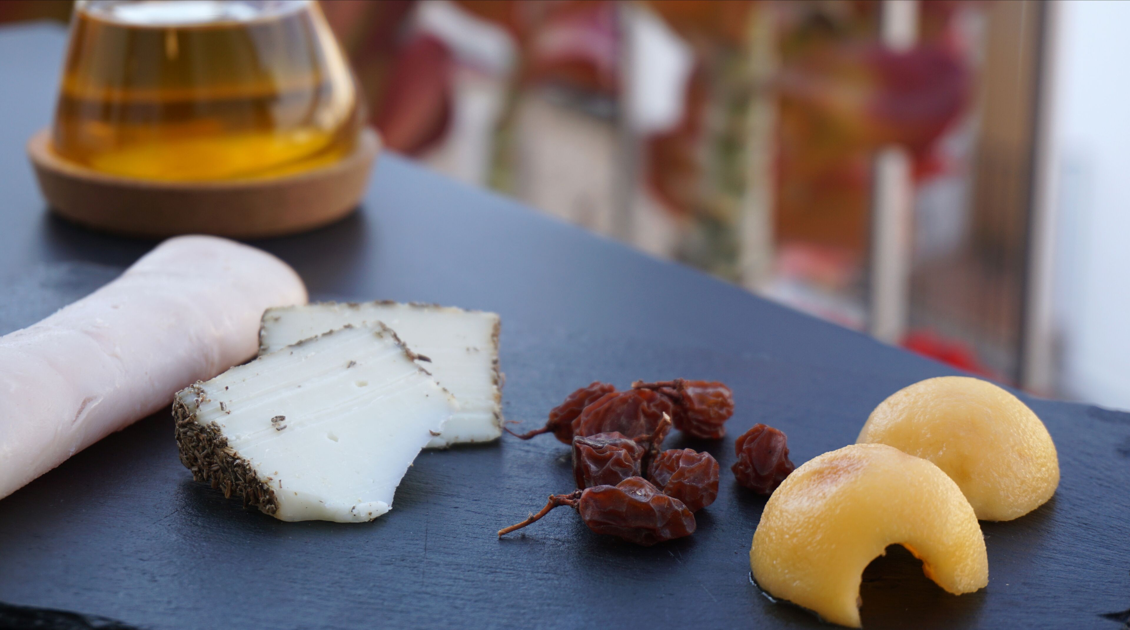 Tagliere con formaggio fresco, frutta secca e una piccola ciotola di miele su una superficie in ardesia.